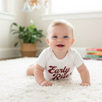 Baby wearing a 'Early Riser' onesie on a white carpet