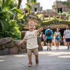 Child wearing a 'Jungle Skipper' shirt pointing at an attraction in a theme park.