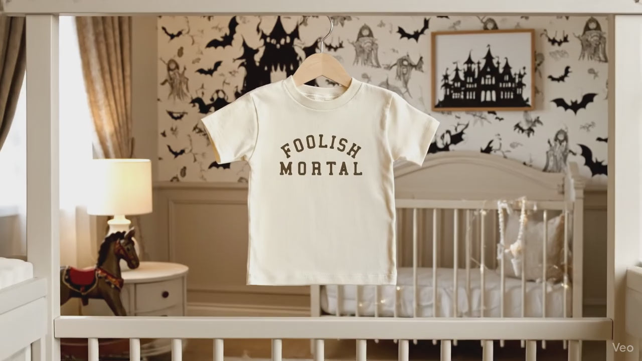 Foolish Mortal Gender Neutral Kids Shirt in a Halloween Theme room with bats 